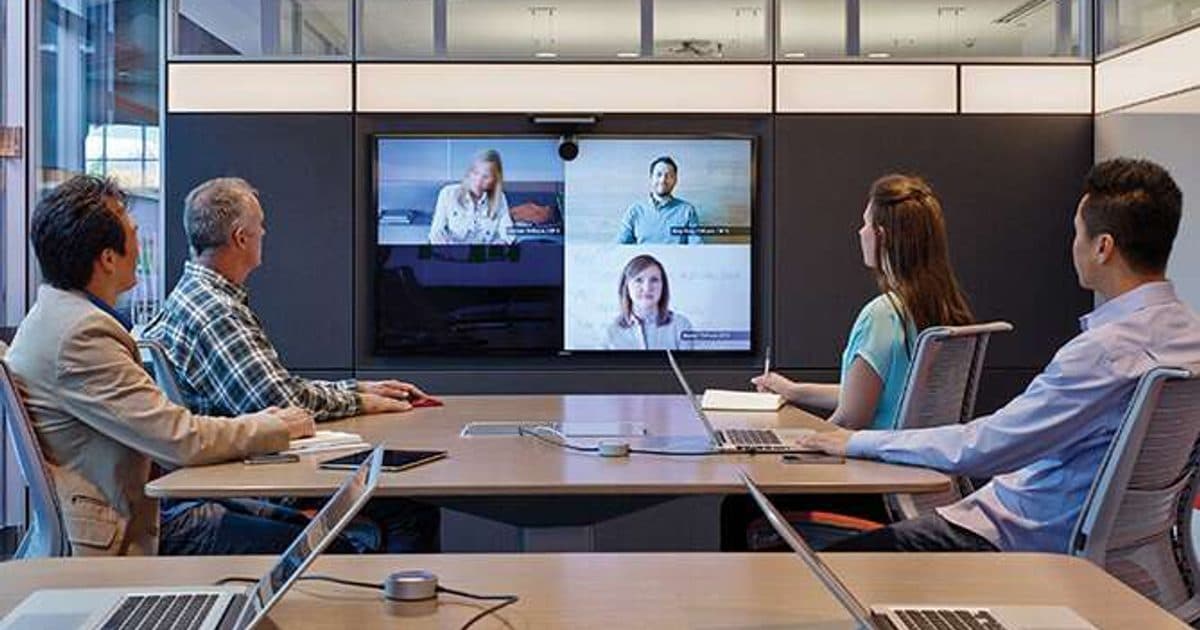 Four people around a meeting table face a screen showing remote participants.