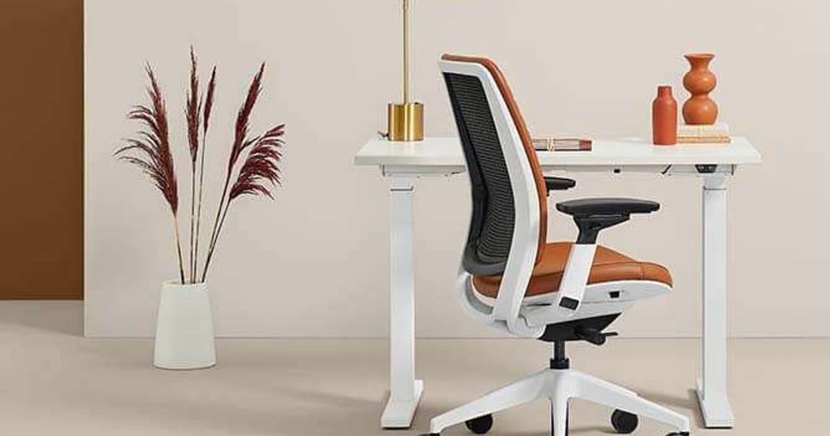 An orange upholstered task chair with a white frame at a height-adjustable desk.