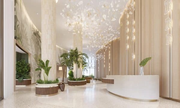 Bright lobby with a terrazzo floor, curved stone reception desk, cascading floral chandelier and planted palms