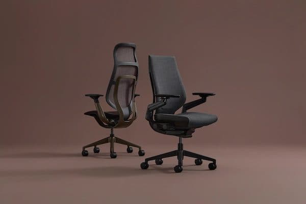 Two ergonomic task chairs, one mesh-backed and one upholstered, posed against a plain warm brown backdrop
