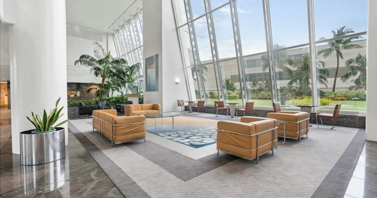 A daylight-filled lobby with tan seating, plants and a large glass wall.