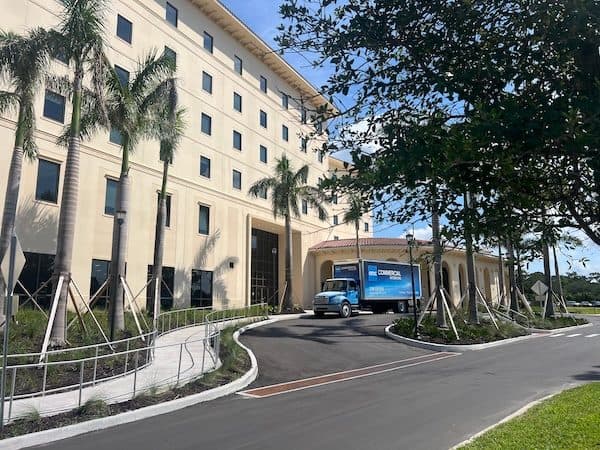 OFDC Commercial Interiors box truck parked at the entrance of a multi-storey campus building framed by palms