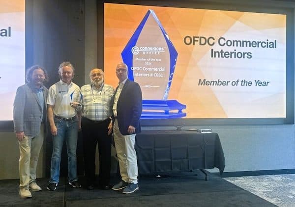 Four men beside a screen reading OFDC Commercial Interiors, Member of the Year, with a glass award on the table