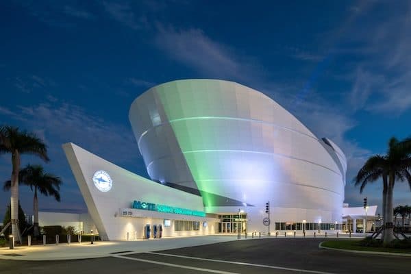 Mote Science Education Aquarium at dusk, its curved white shell facade lit green and blue above the entry canopy