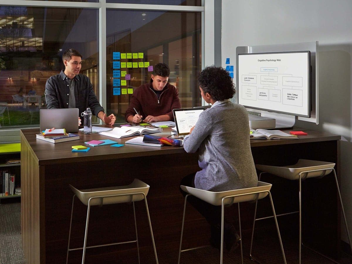 Three people working at a Steelcase media:scape table with a shared monitor