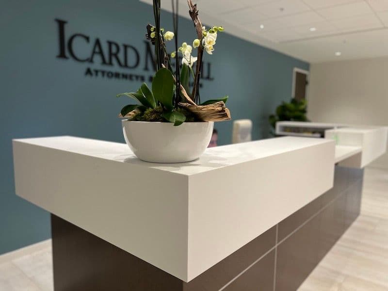 Detail of white-orchid arrangement in white bowl on reception counter; blurred Icard Merrill blue brand wall behind.