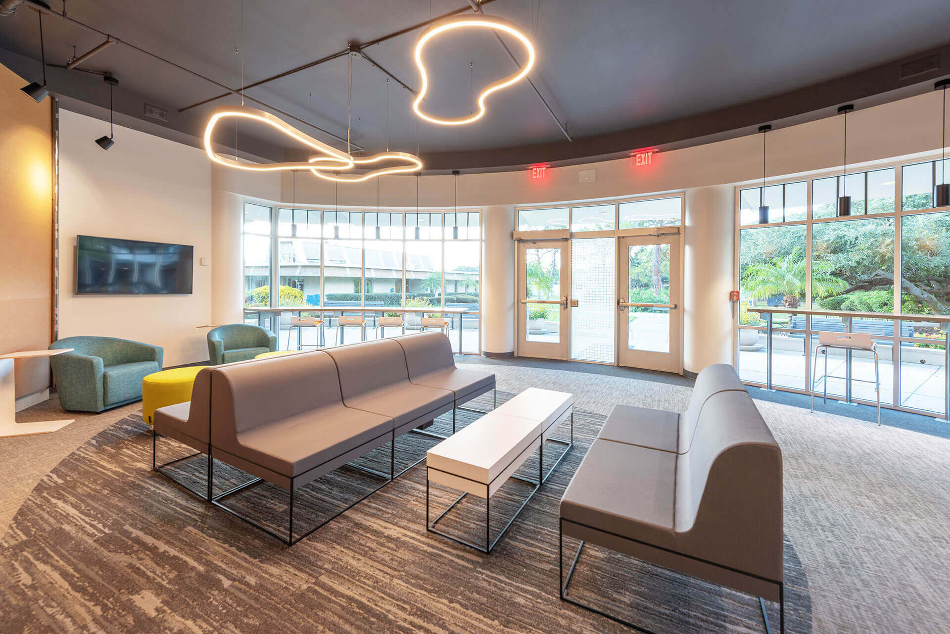 A lobby with 3 benches and 2 chairs in front of doors leading outside OFDC Commercial Interiors