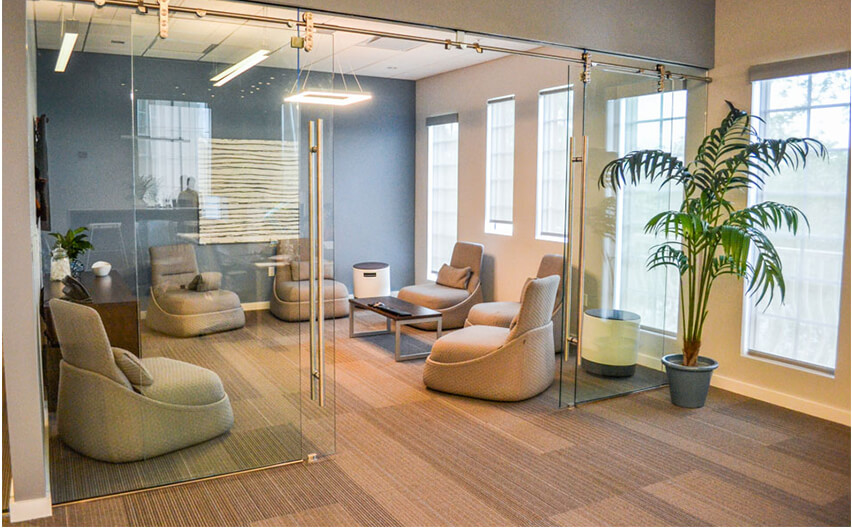A lounge area with 6 chairs and a low top coffee table inside of an office with glass sliding doors by OFDC Commercial Interiors