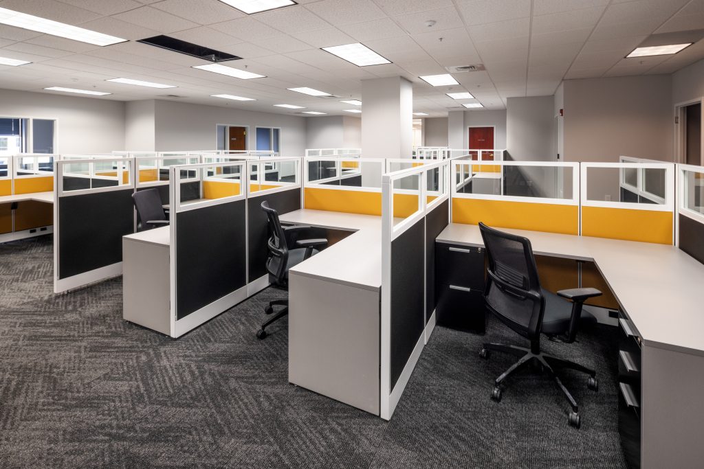 A bright, empty office with open cubicles and carpet flooring.